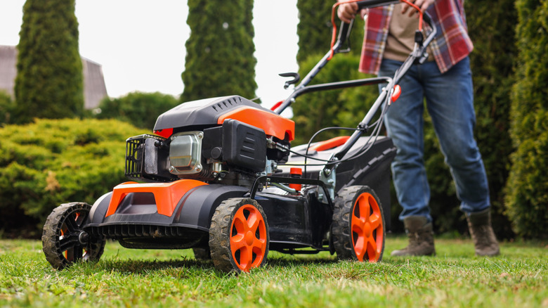 An orange and black lawnmower being pushed across a yard.