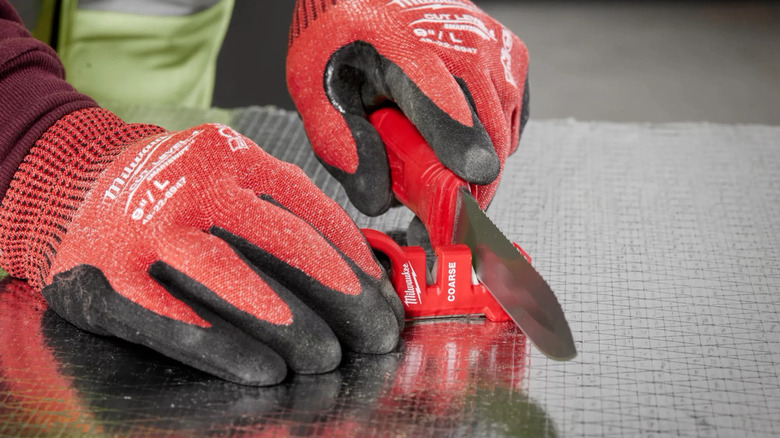 a person using the Milwaukee handheld knife sharpener on a metal bench