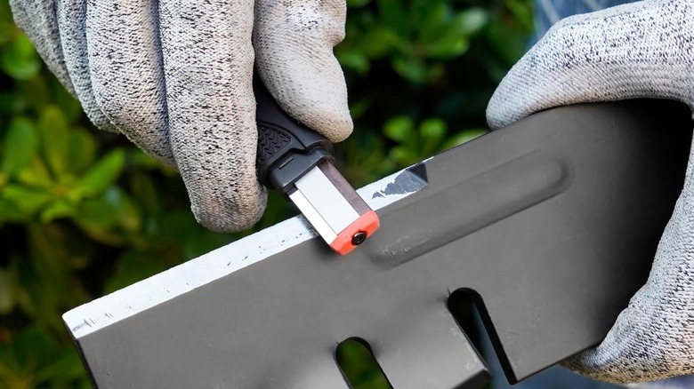 Gloved hands using SHARPAL 129N Multipurpose Garden Tool Blade Sharpener to sharpen a blade