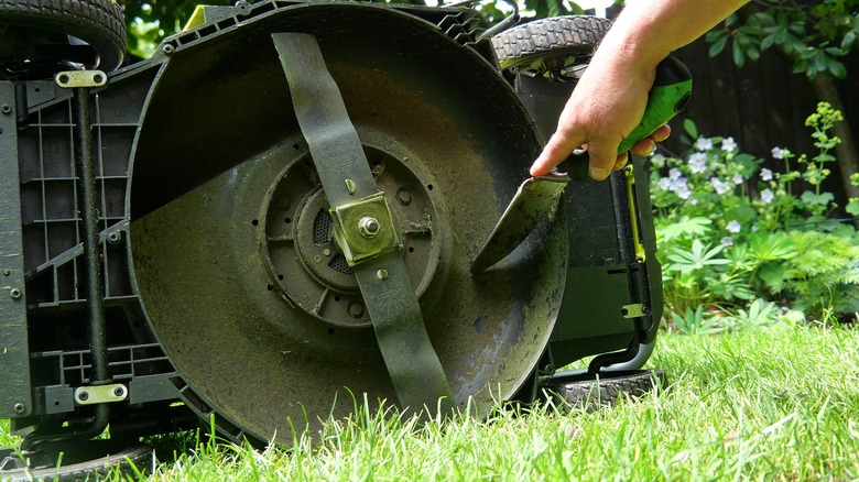 Hand pointing at the blade attached to the underside of a lawn mower