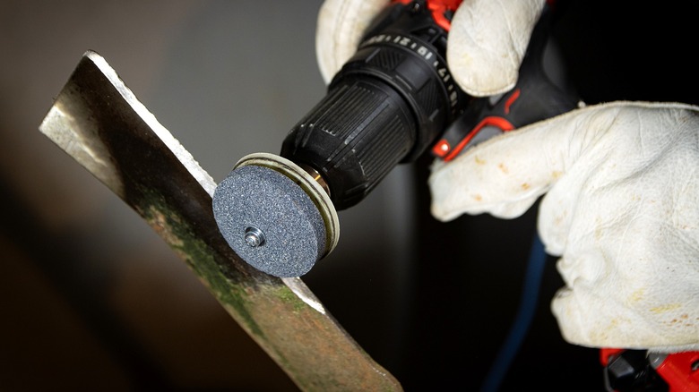 Gloved hands using a power drill stone attachment to sharpen a lawn mower blade