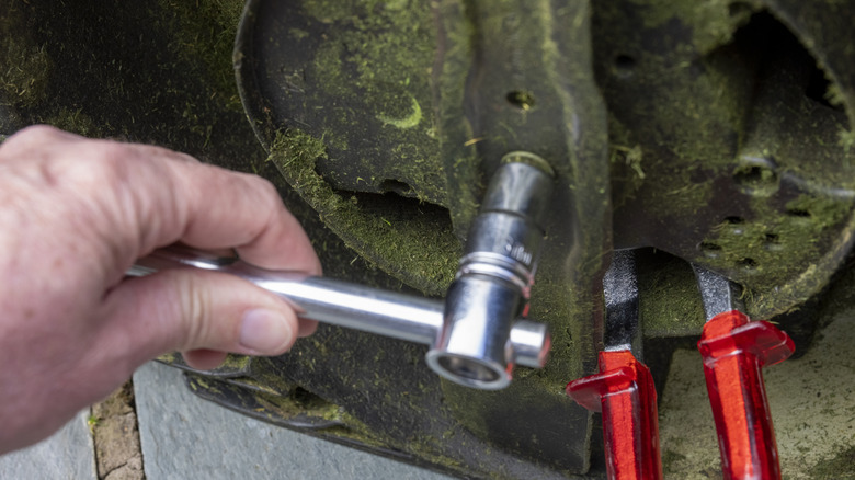 Man removing a lawn mower blade with a socket wrench