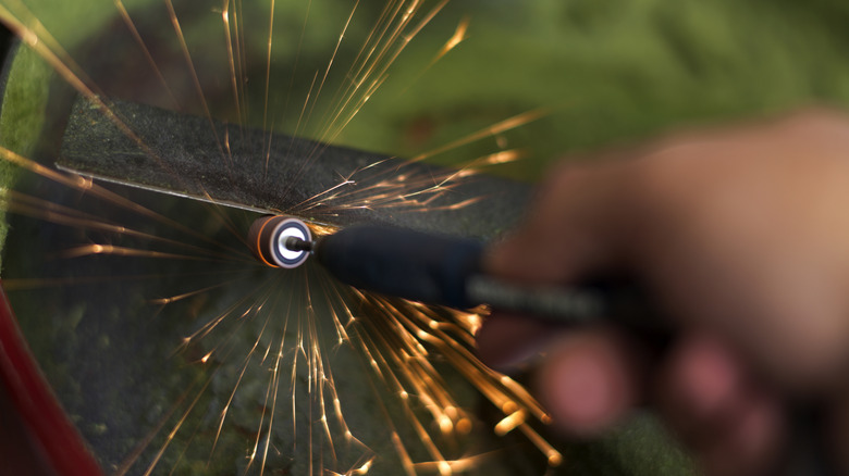 Person sharpening lawn mower blade on a rotary grinder