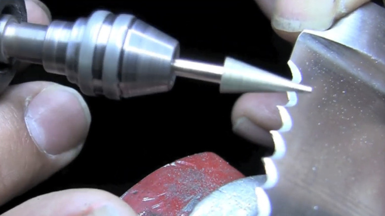 Close-up showing a person sharpening a serrated knife with a rotary tool