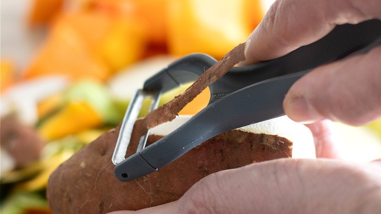 Close-up of a person's hands peeling a potato with a black Y-shaped vegetable peeler