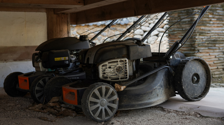 Lawn mowers stored under a wooden structure.