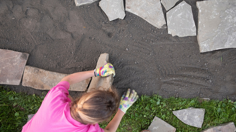 Woman laying down pavers on dirt patio