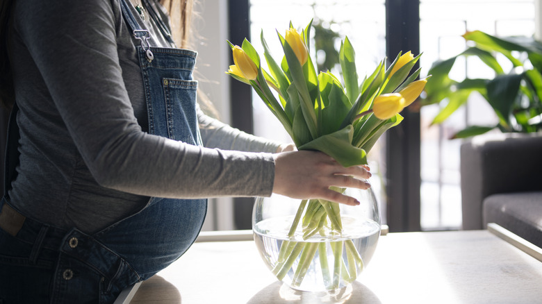 Woman touching flowers in a glass vase filled with water.