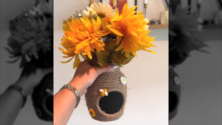 Woman's hand holding DIY bee hive vase with yellow flowers.