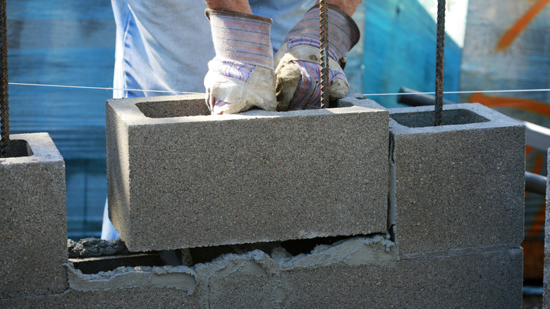 Gloved hands placing a concrete block over rebar on prepared mortar.