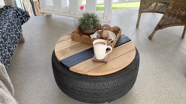 DIY patio table made from a tire and a wooden tabletop, with a cup of coffee and a wicker tray on top