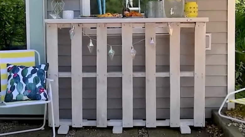 A white bar counter made out of wooden pallets used as a buffet station on a stone patio.