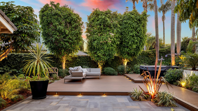 A wood floating backyard deck sits in front of a lush garden.
