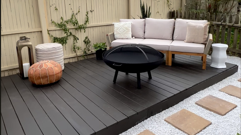 White patio furniture and a black firepit sit on a black floating wood deck.