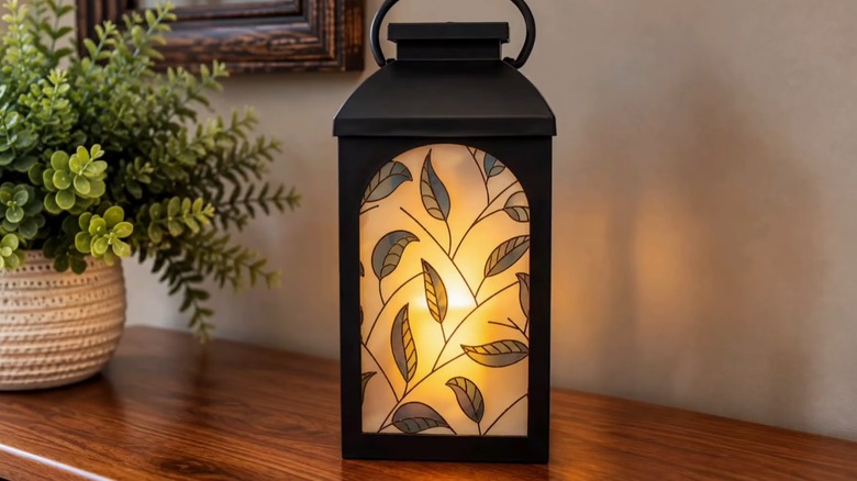 A faux stained glass lantern with the light turned on sits on a wooden living room console.