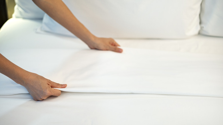 Close-up of a person adjusting clean white sheets on a neatly made bed