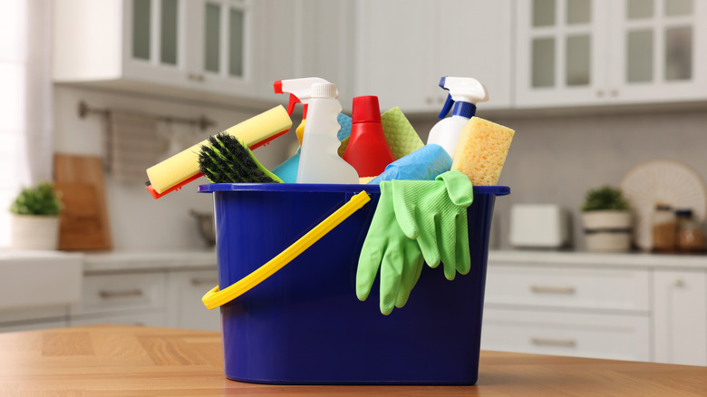 A bucket filled with cleaning products and tools sitting on a bench in the kitchen