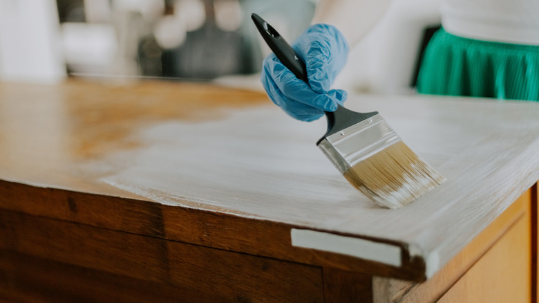 Close up of woman painting the top of a wooden furniture piece white