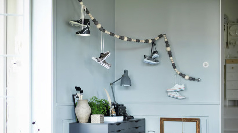 A curtain wire covered with wooden balls in the corner of a room with sneakers hung over it by their laces.