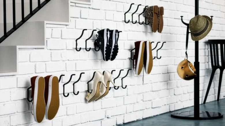 Hooks attached to a white painted brick wall with shoes hung off them, with a hat and bag stand next to them.