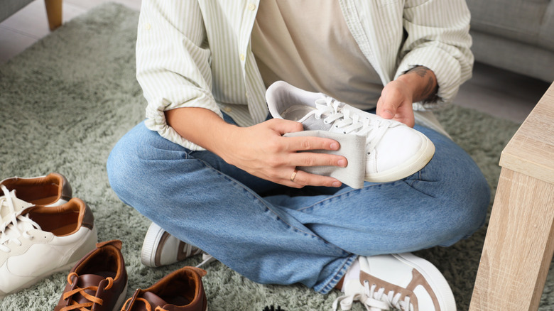 Young man cleaning white sneaker at home, closeup