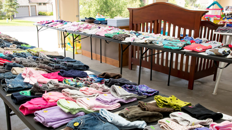 A garage sale with lots of clothing, a crib, and other kids' items
