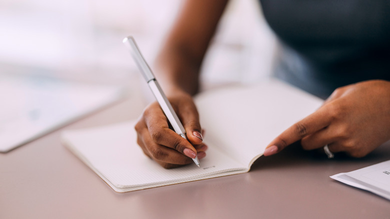 Person writing a list in a small notebook