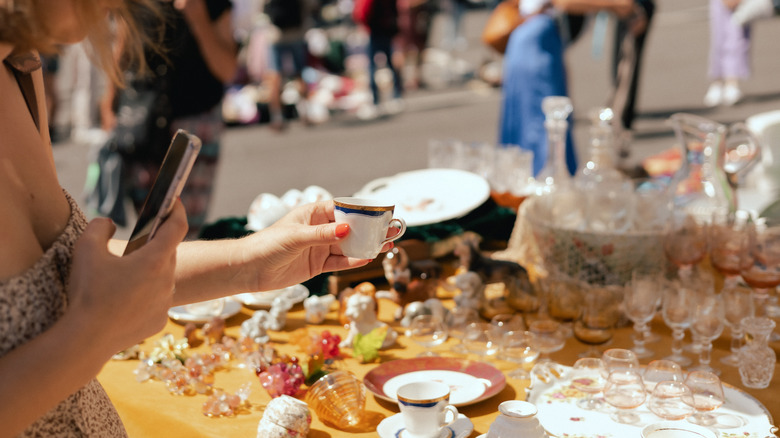 Woman taking a photo of a vitage cup at a yard sale