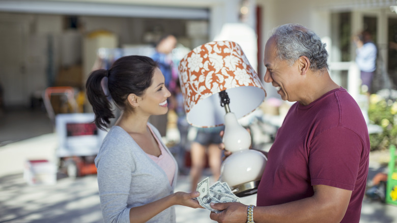 Man holding a lamp at a garage sale and handing a woman money