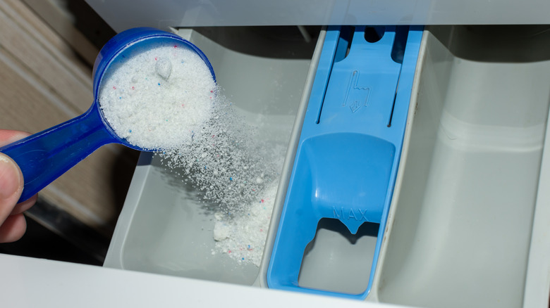 Someone pours powder laundry detergent into a washing machine dispenser