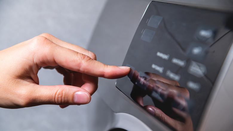Hand pressing a button on a washing machine panel