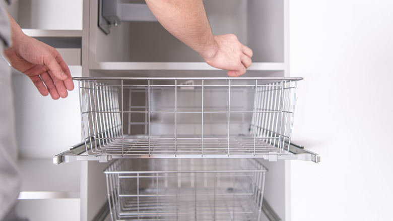 Hands pulling out a wire basket from a cabinet.