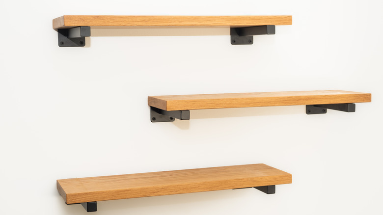 Thick wooden Shelves made by natural oak planks mounted with black steel bracket attachments to wall.