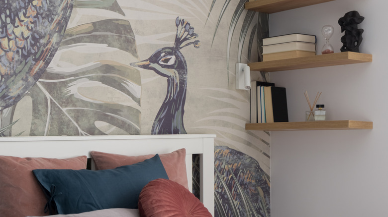 Charming bedroom with comfortable bed with nice bedclothes, stylish wallpaper and simple wooden floating shelves with books and decorations.