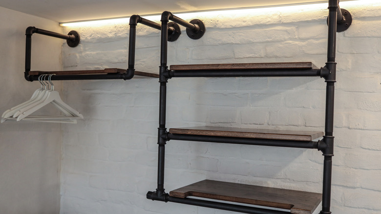 Modern industrial wall shelves made of black pipes and dark wood with white hangers, mounted on a white brick wall under LED strip lighting.