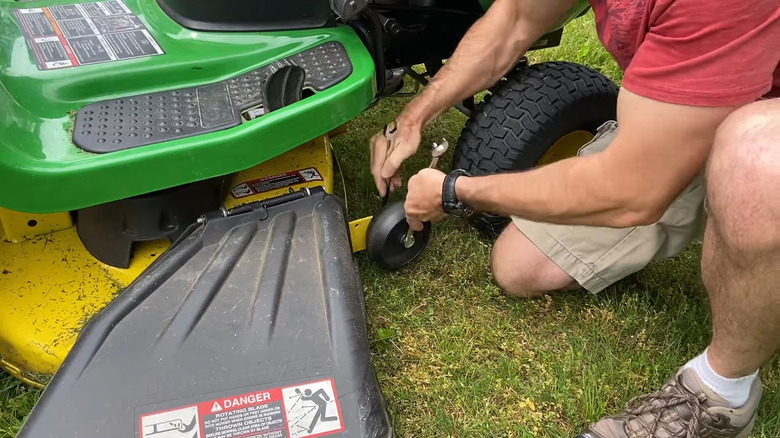 a man adjusts the height of the mower deck wheels of his riding lawn mower