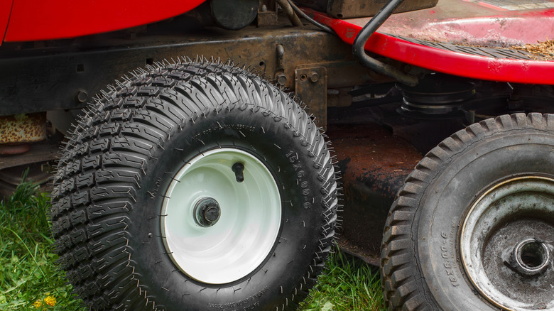 A brand new wheel on a lawn tractor, with the old wheel on the side