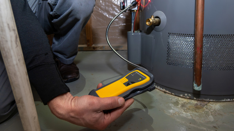 A worker uses a device to test carbon monoxide output from a water heater.