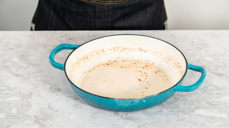 A blue and white enamel cast iron pan with food stains sits on a faux marble countertop.