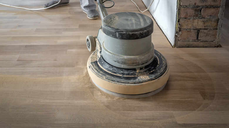 A round hardwood floor sander with sawdust surrounding the base.
