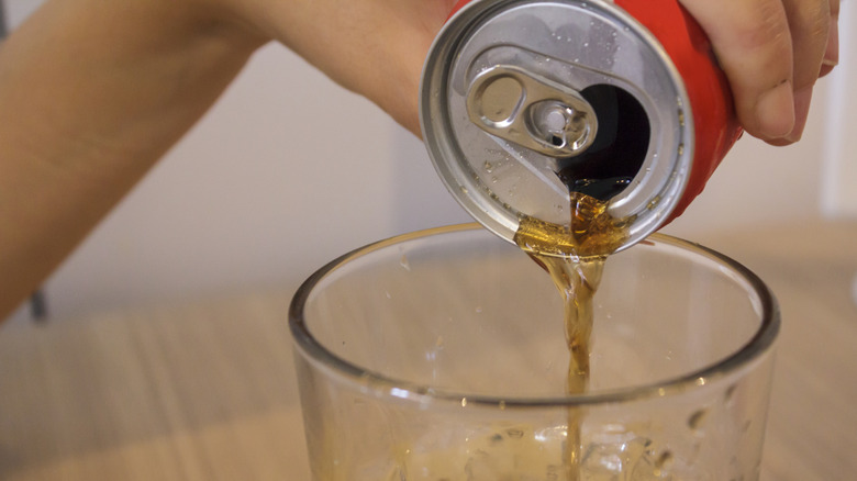 Hand pouring a can of cola in clear glass
