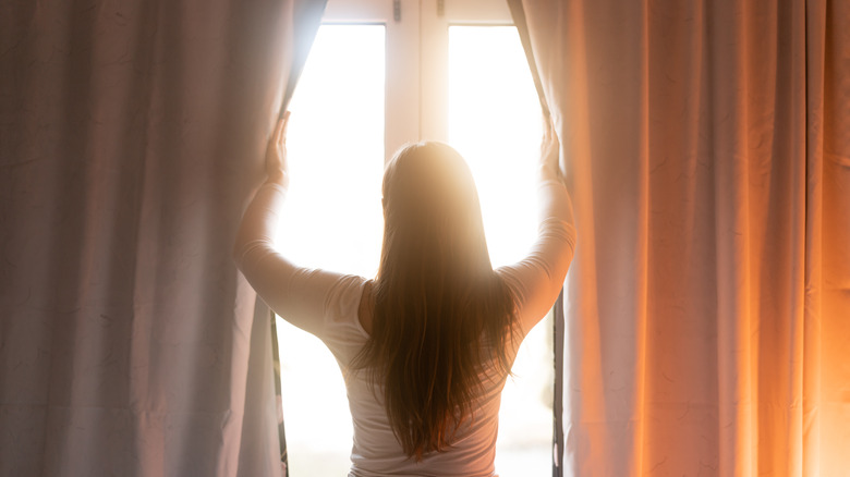 Rear view of a woman opening curtains