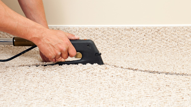 A man using a carpeting black carpeting tool to install beige Berber carpet.