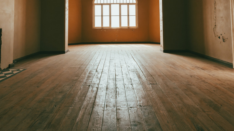 A room with natural light shining on old hardwood floors with old cracked walls.
