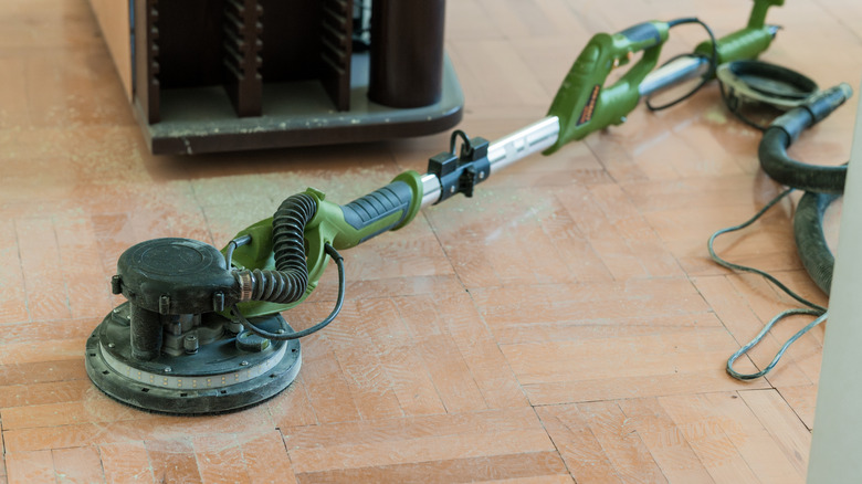 A green, round wood floor sanding machine laying on an old hardwood floor.