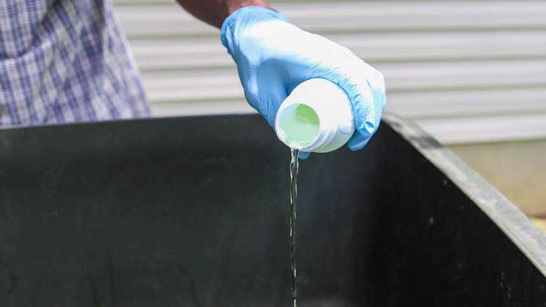 Gloved hand pouring bleach into trash can