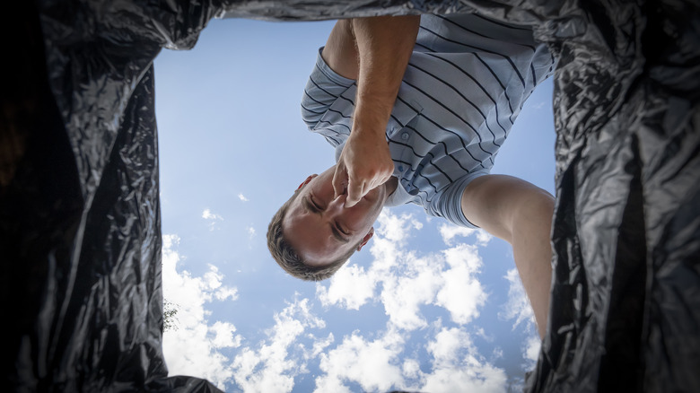 Man leaning over smelly trash can