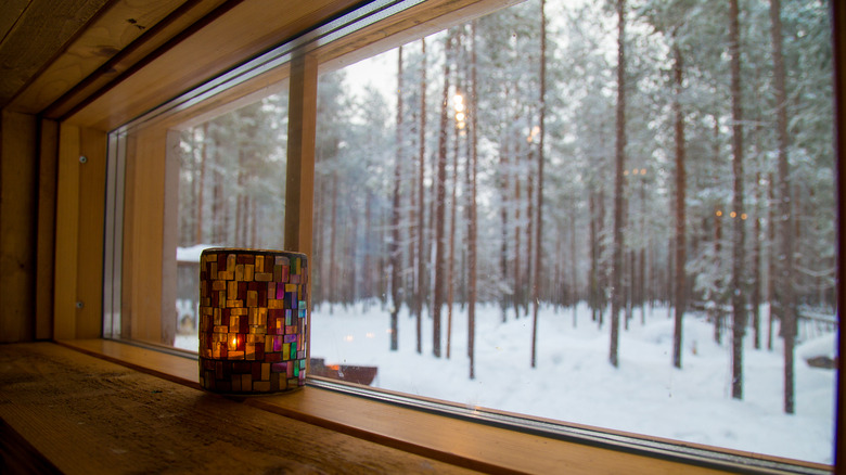 The view of a snowy landscape through a large window with a candle sitting on the timber sill