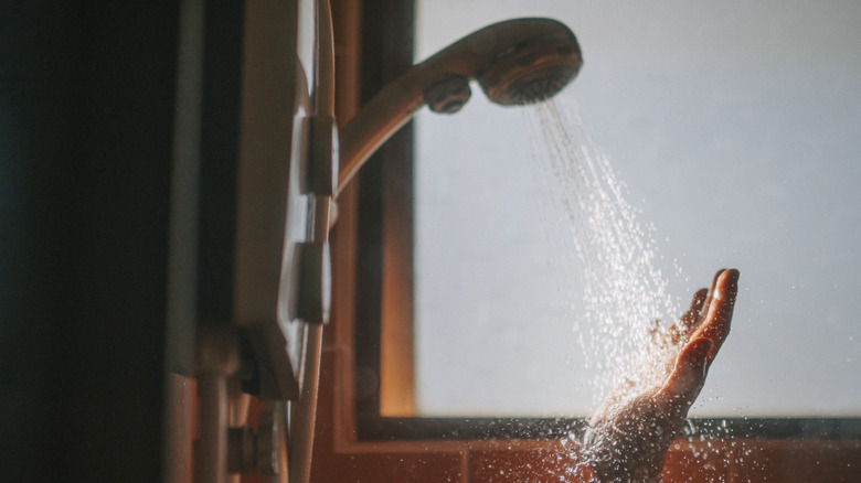 A person feeling the water pressure of a shower with their hand
