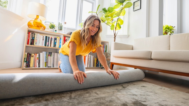 Woman rolling up area rug in front of cream sofa